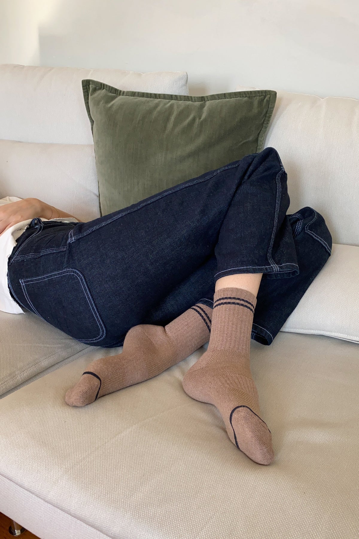 Person wearing brown socks with black stripes sitting on a beige couch with green pillow