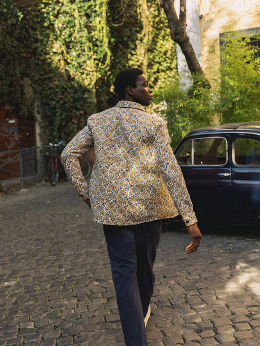 Male model walking on cobblestone street wearing David Devea overshirt clear blue floral pattern navy pants