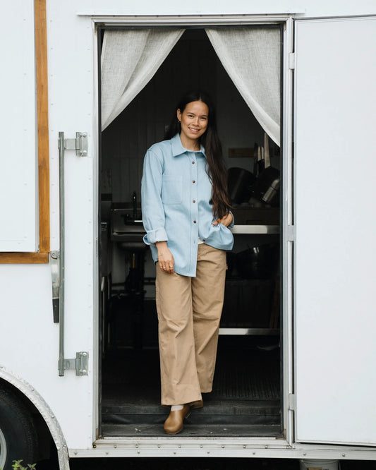 FULL FEMALE MODEL SHOT, STANDING IN WHITE TRAILER DOORWAY WEARING A LIGHT BLUE DENIM SHIRT, SMILING, WITH LONG DARK HAIR
