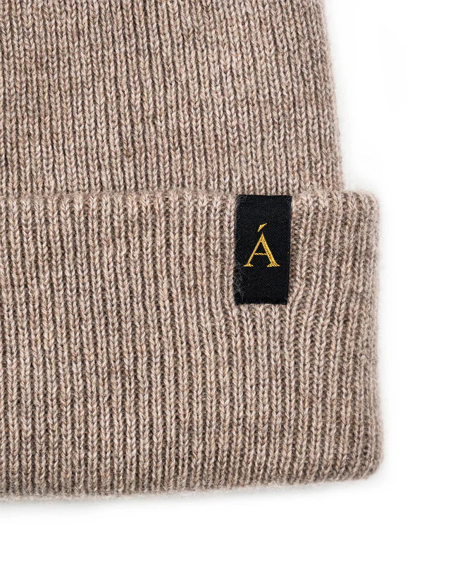 Anian beanie ribbed knit cuffed winter hat in taupe with black woven logo tag closeup on textured fabric in Kelowna