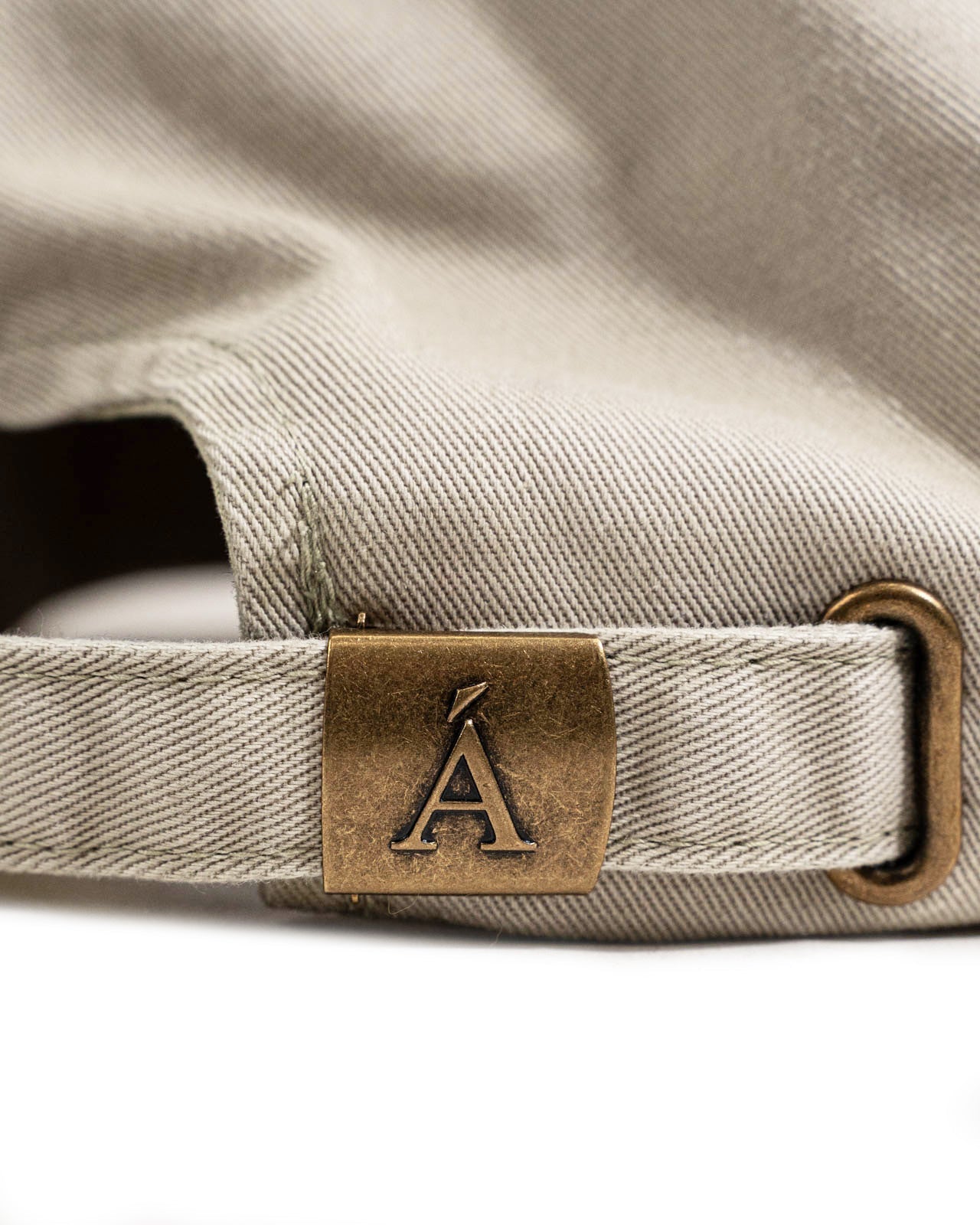 Close up of beige cotton hat back showing adjustable strap and brass clasp engraved with logo in Kelowna