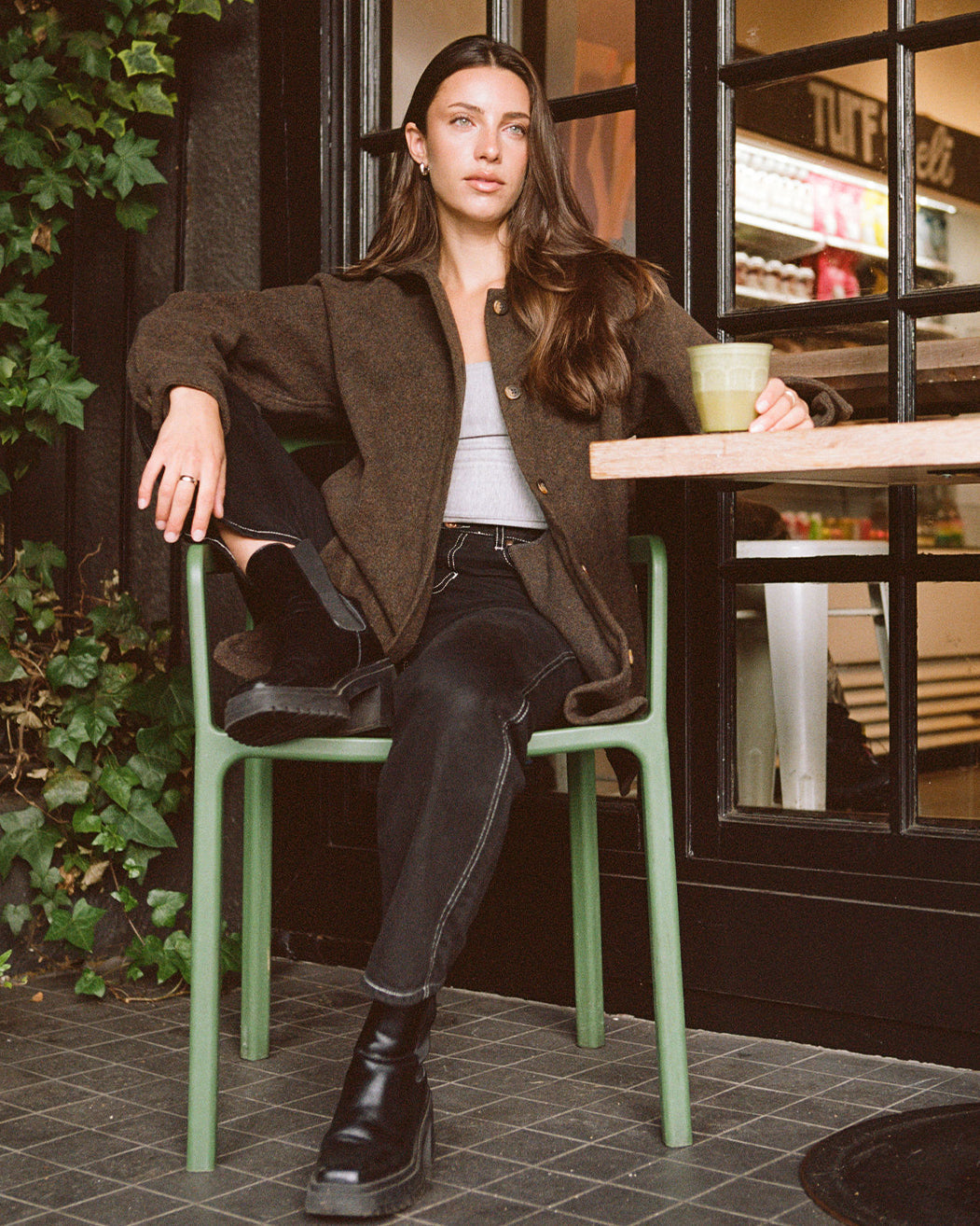 Anian loft coat in brown wool style modeled by woman sitting at cafe wearing black jeans and boots in Kelowna