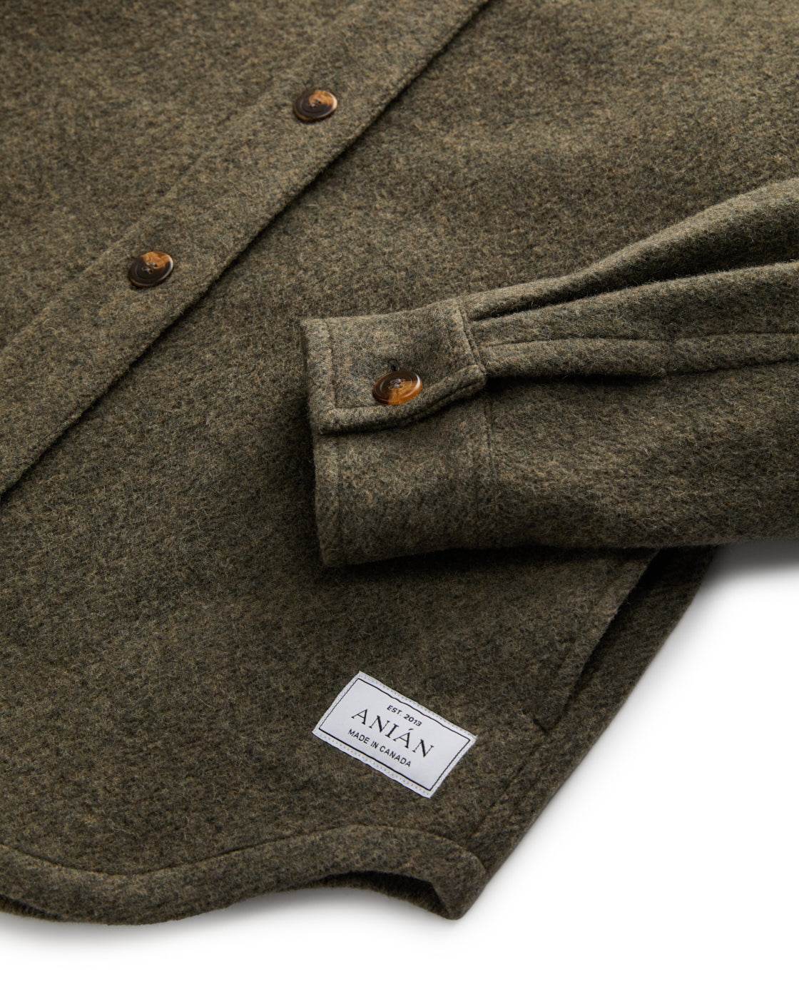 Anian olive wool loft coat closeup showing textured fabric folded sleeve button cuff and brand label in Kelowna
