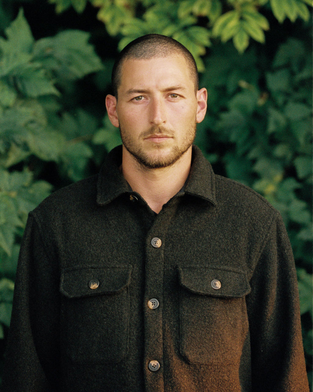 Anian mens wool coat in dark olive with button front and flap chest pockets on male model outdoors in Kelowna