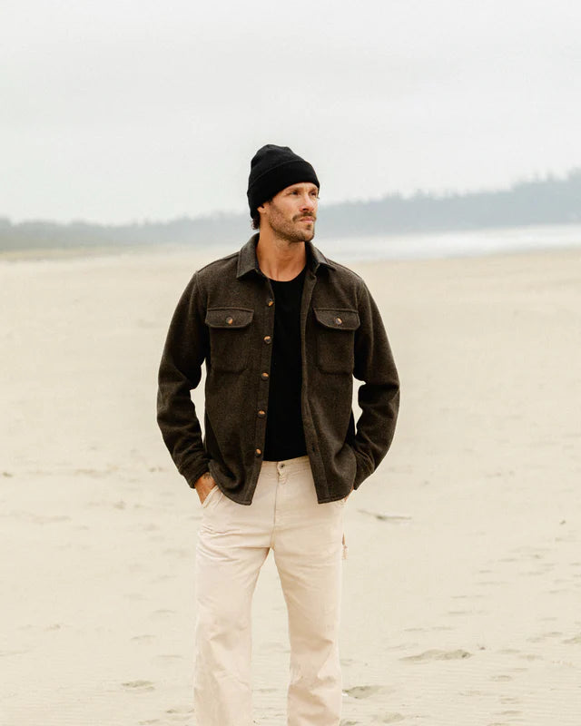 Anian mens wool coat in dark brown worn by model on a foggy beach with beanie and cream pants in Kelowna
