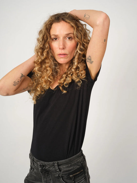 Black MOS MOSH Canada v-neck tee on curly blonde model with tattoos, tucked into faded black jeans in Kelowna