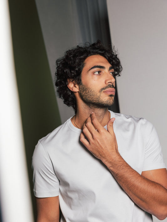 Male model with curly hair wearing organic gray t-shirt looking sideways with hand at neck in Kelowna