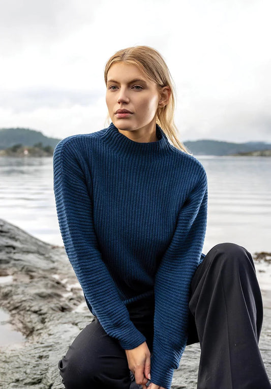 woman outside near water in a blue merino wool sweater