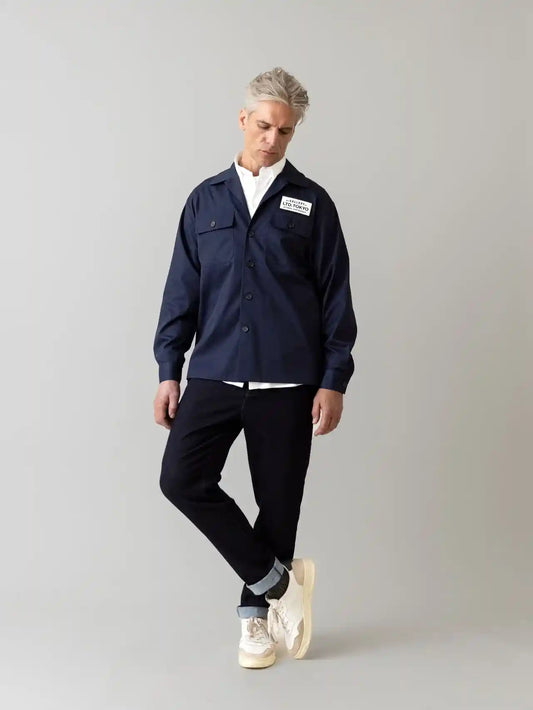 Mos Mosh Gallery Hunt Comfy Pant - Man wearing a navy blue jacket with a logo, white shirt, black pants, and white sneakers on a gray background