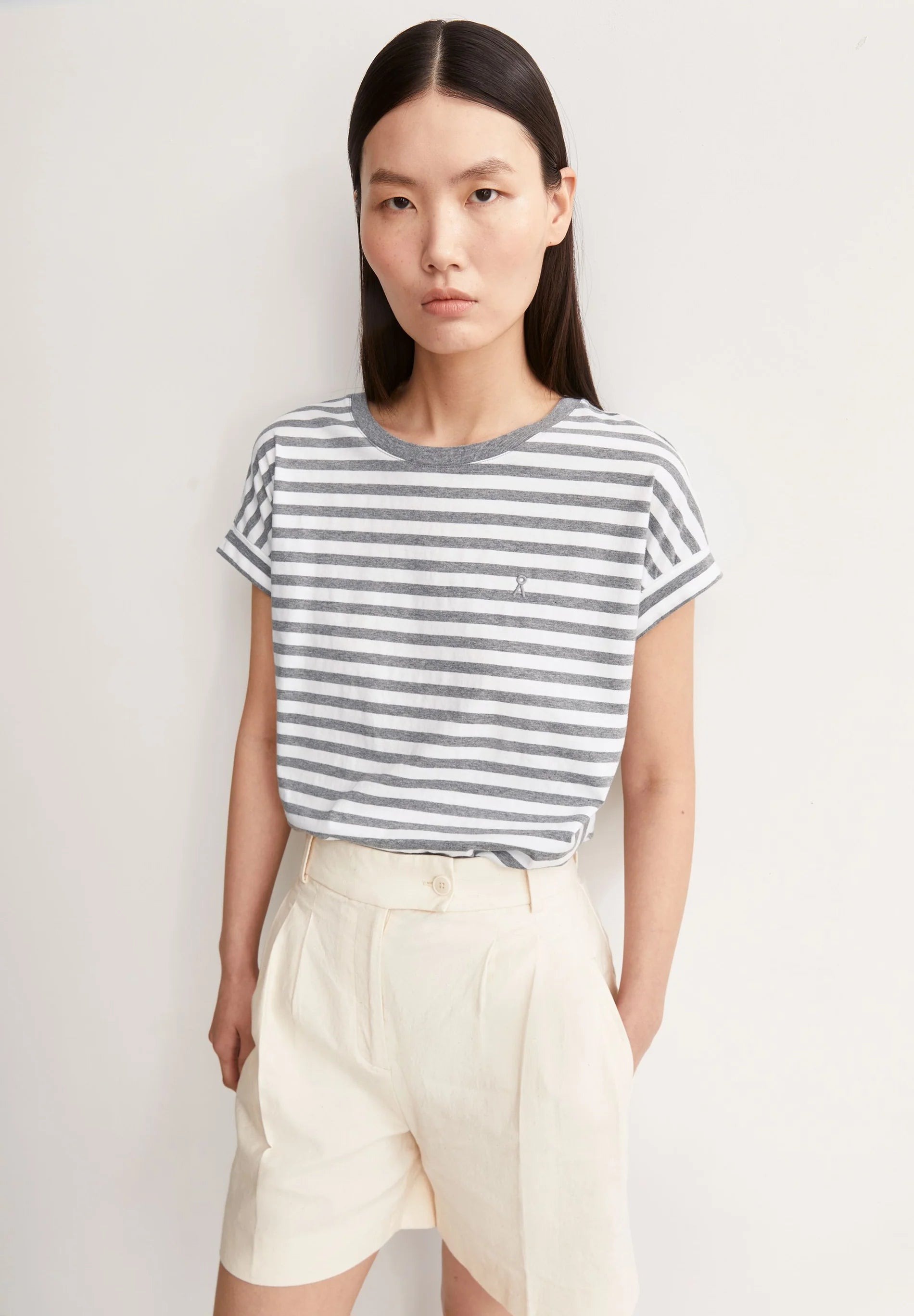 Woman wearing a striped t-shirt and beige shorts against a plain background