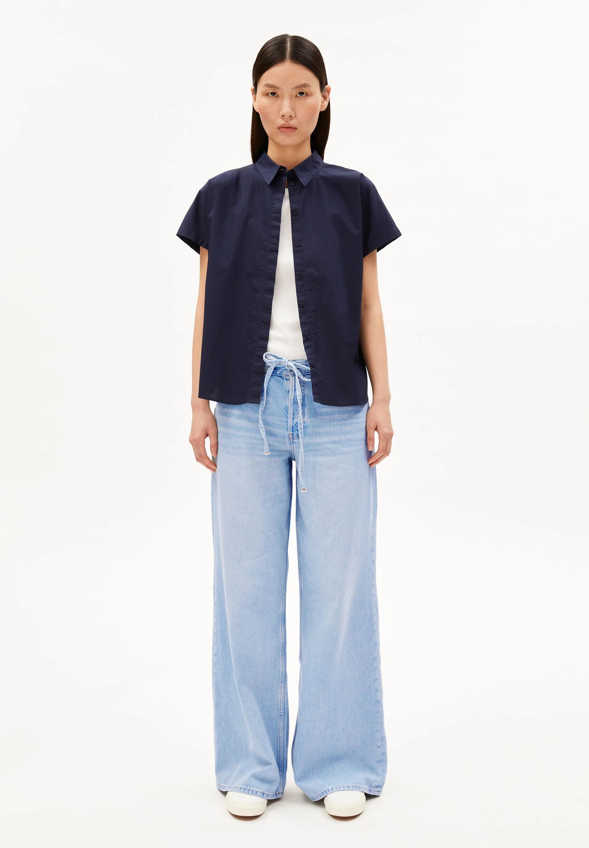 Woman wearing a navy shirt, white top, and light blue jeans on a white background for Kelowna and Canada