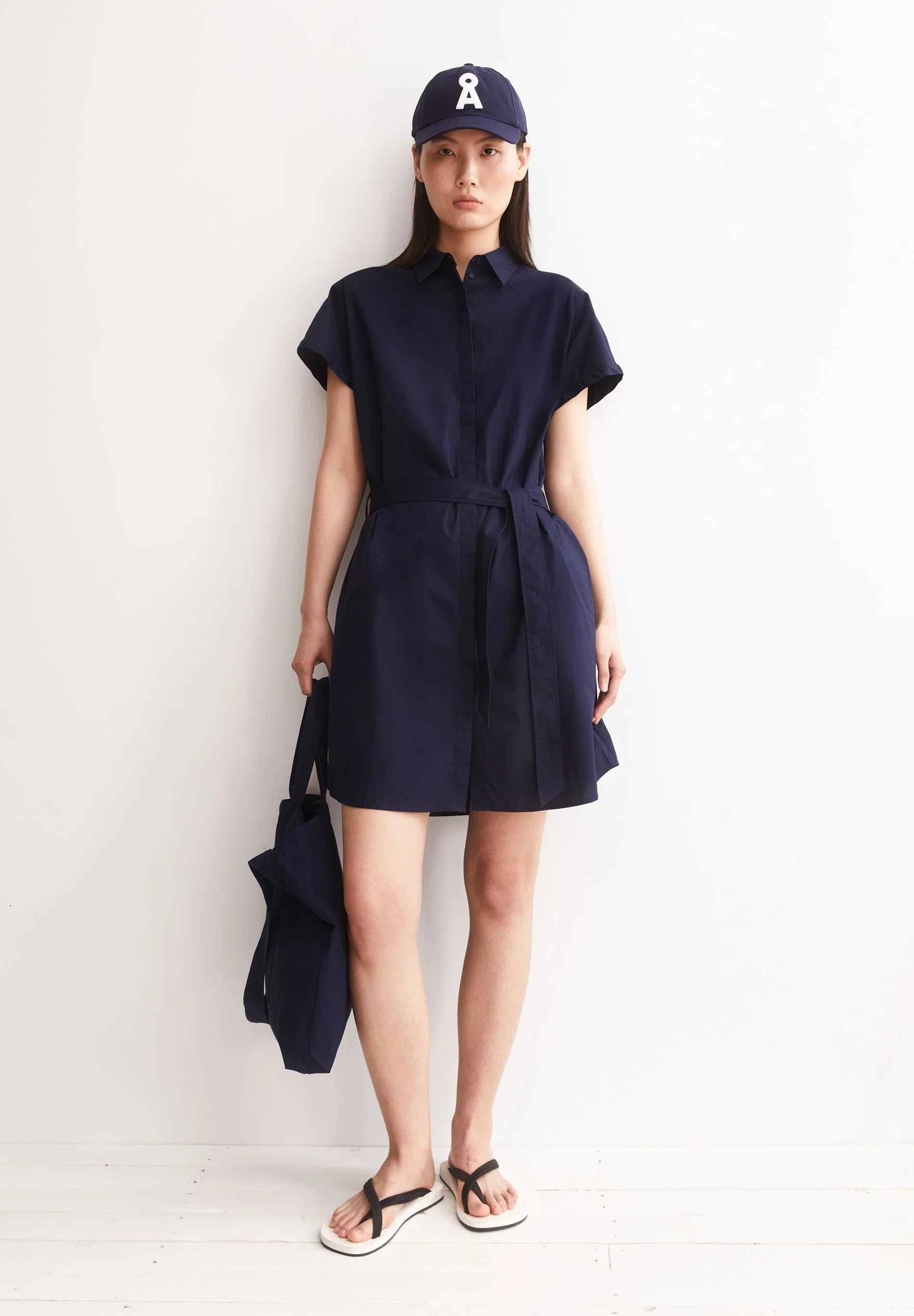 ARMEDANGELS LARISAANA Poplin Mini Dress in Tinted Navy, front studio shot with bag and hat on model in Kelowna, organic cotton