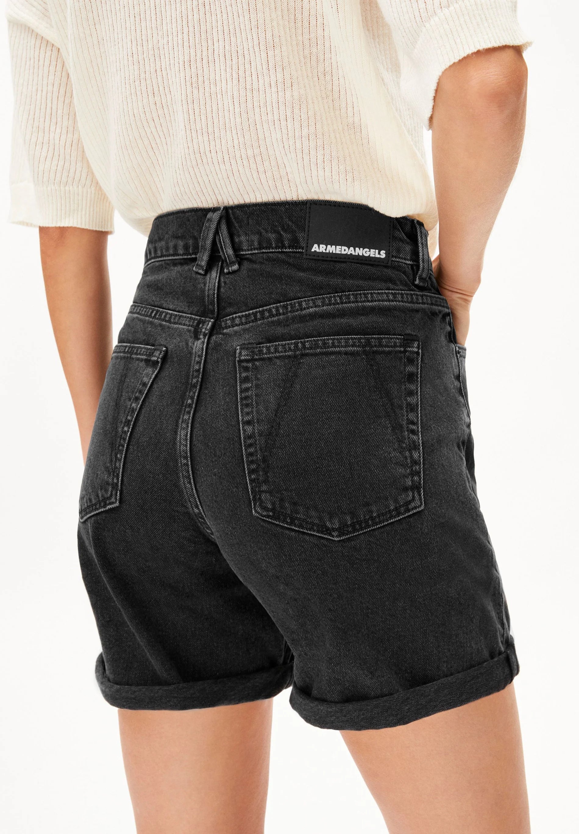 Close up back side of person wearing black denim shorts with brand label on a white background for Kelowna and Canada
