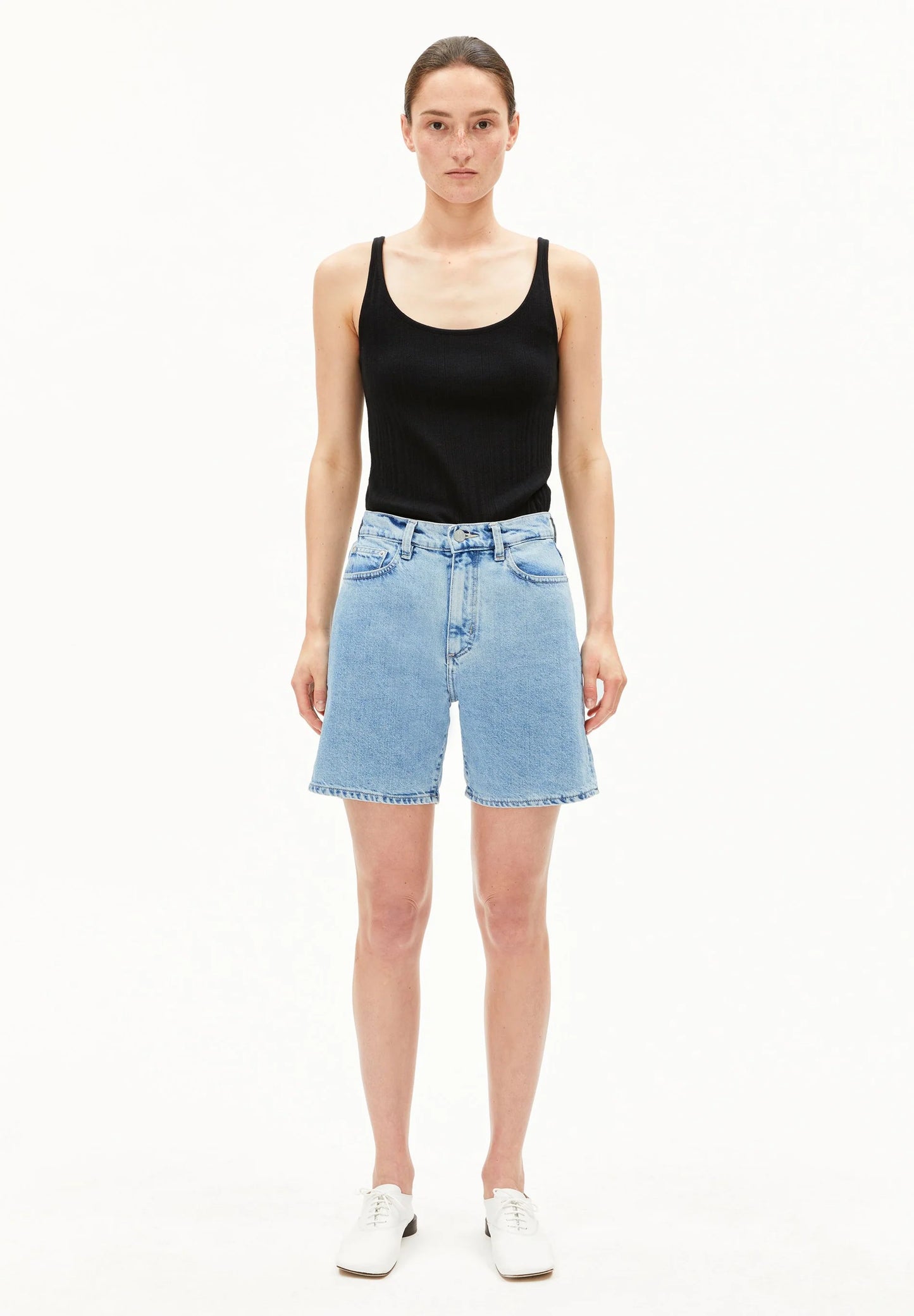 Woman wearing a black tank top and light blue denim shorts on a white background for Kelowna and Canada