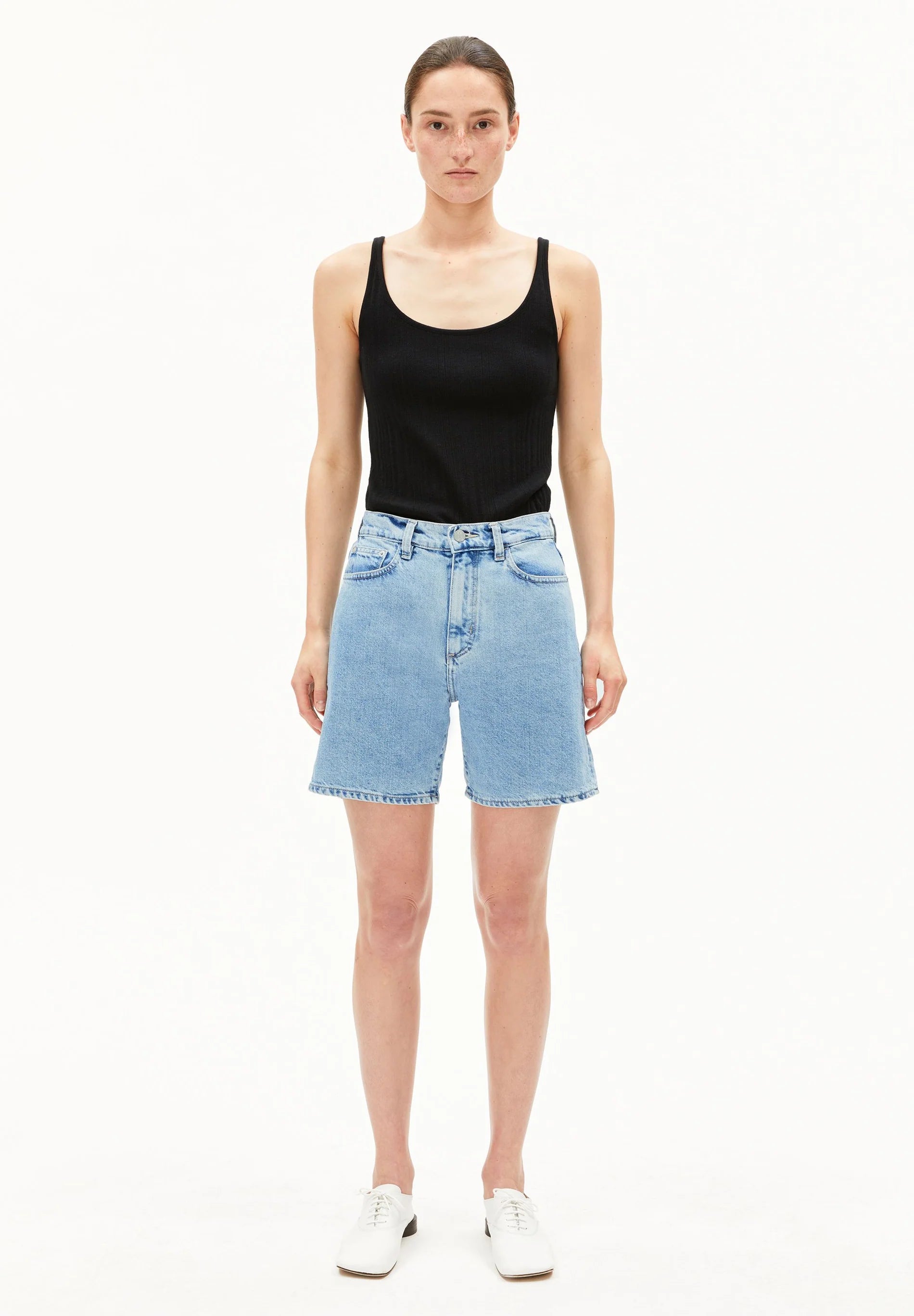 Woman wearing a black tank top and light blue denim shorts on a white background for Kelowna and Canada