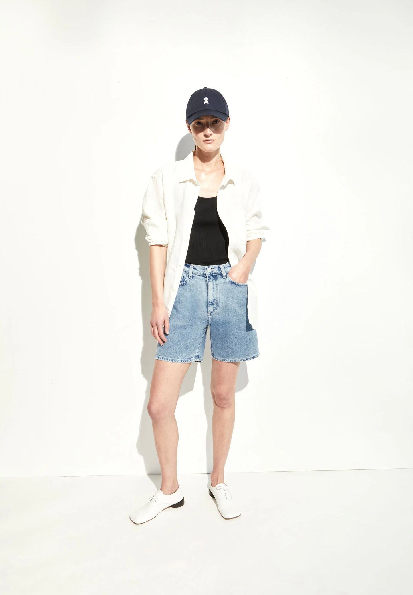 Person wearing a white shirt, black tank top, blue denim shorts, and a navy cap on a white background for Kelowna and Canada