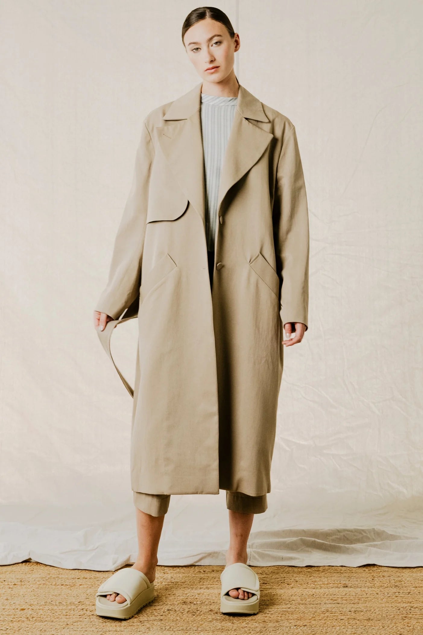 Front view showing belt detail on model of District Trench Coat in Beige by Bodybag by Jude — oversized Tencel-cotton trench with removable belt, available in Kelowna at Textile Apparel