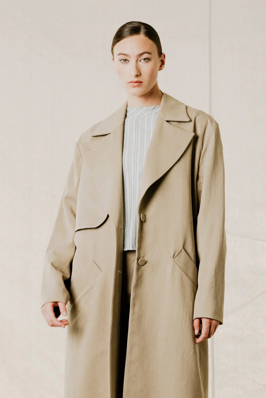 mide range front view on model of District Trench Coat in Beige by Bodybag by Jude — oversized Tencel-cotton trench with removable belt, available in Kelowna at Textile Apparel

