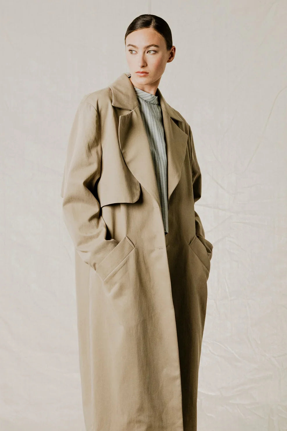 Side view on model of District Trench Coat in Beige by Bodybag by Jude — oversized Tencel-cotton trench with removable belt, available in Kelowna at Textile Apparel

