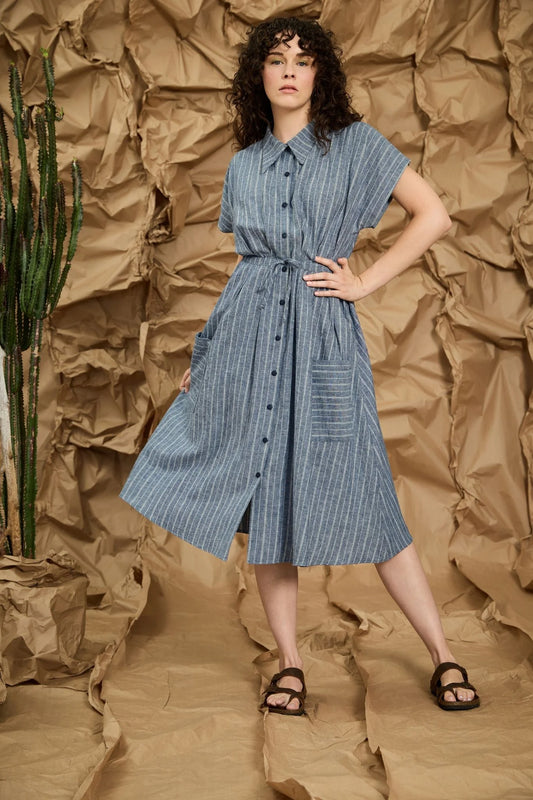 Woman wearing a blue dress standing against a textured brown background in Kelowna 