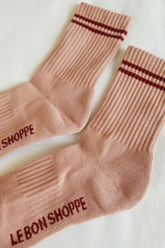 Pair of brown socks with red stripes and 'Le Bon Shoppe' branding on a light background