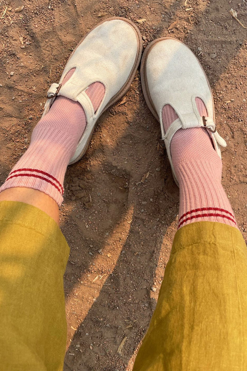 White loafers, pink socks with red stripes, and yellow pants on a dirt ground.