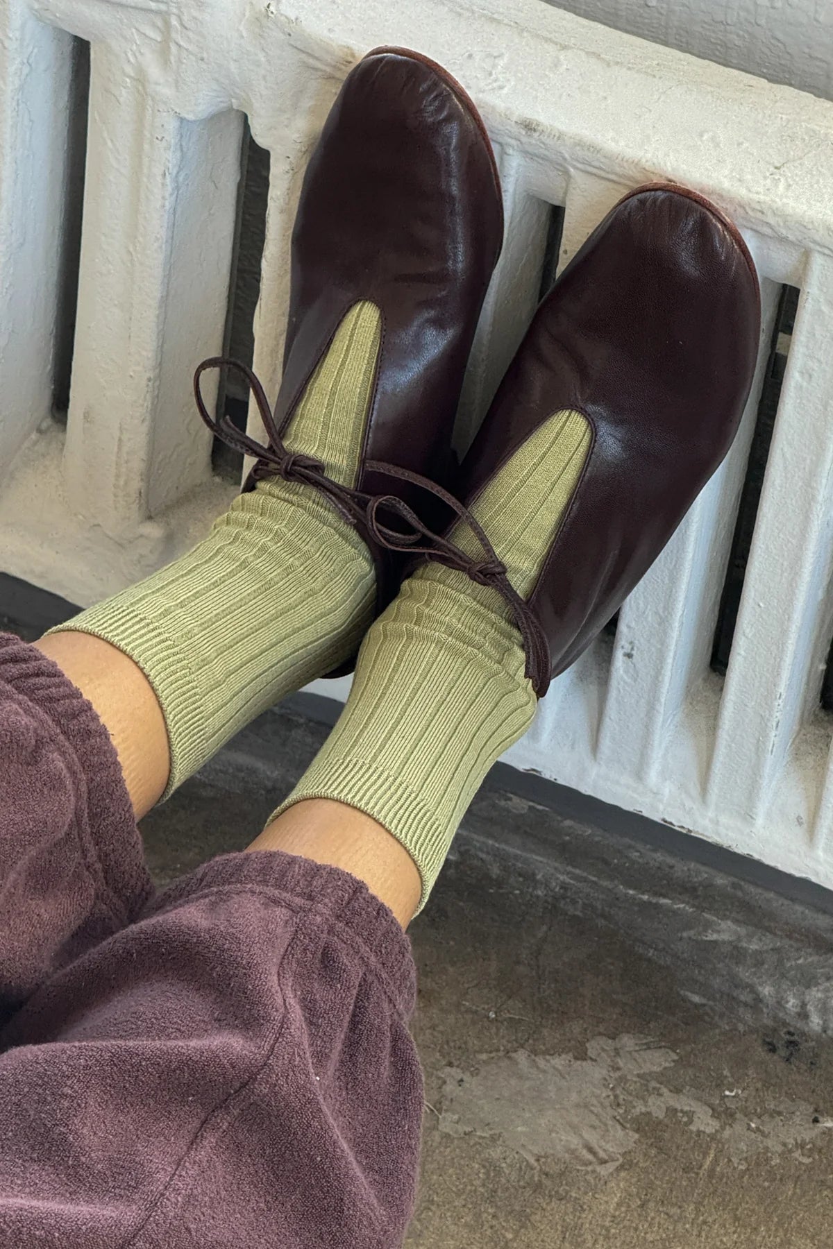 Green socks being worn, with brown leather shoes with a white railing in the background.