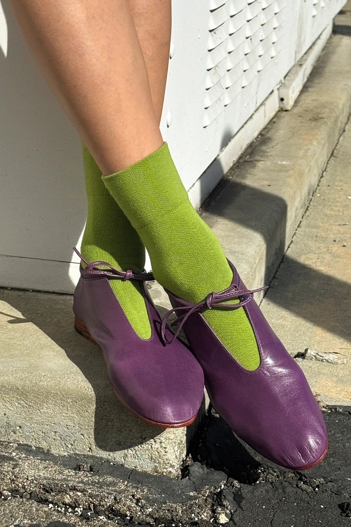 Purple shoes and green socks worn by a person on a concrete step.