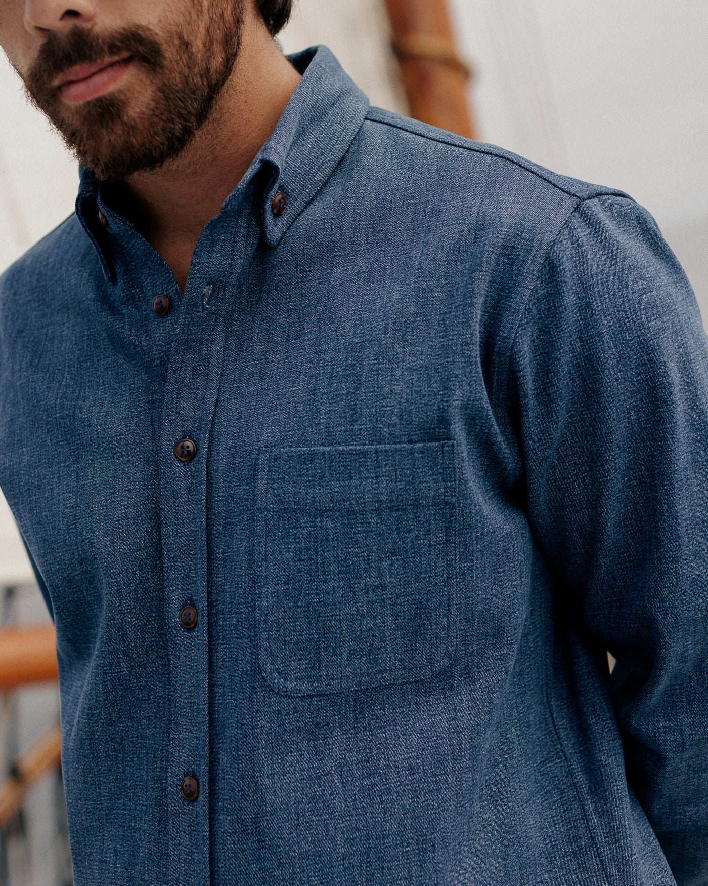CROPPED PHOTO OF MALE MODEL WEARING DARK BLUE DENIM SHIRT, DETAIL SHOT OF COLLAR AND FRONT POCKET