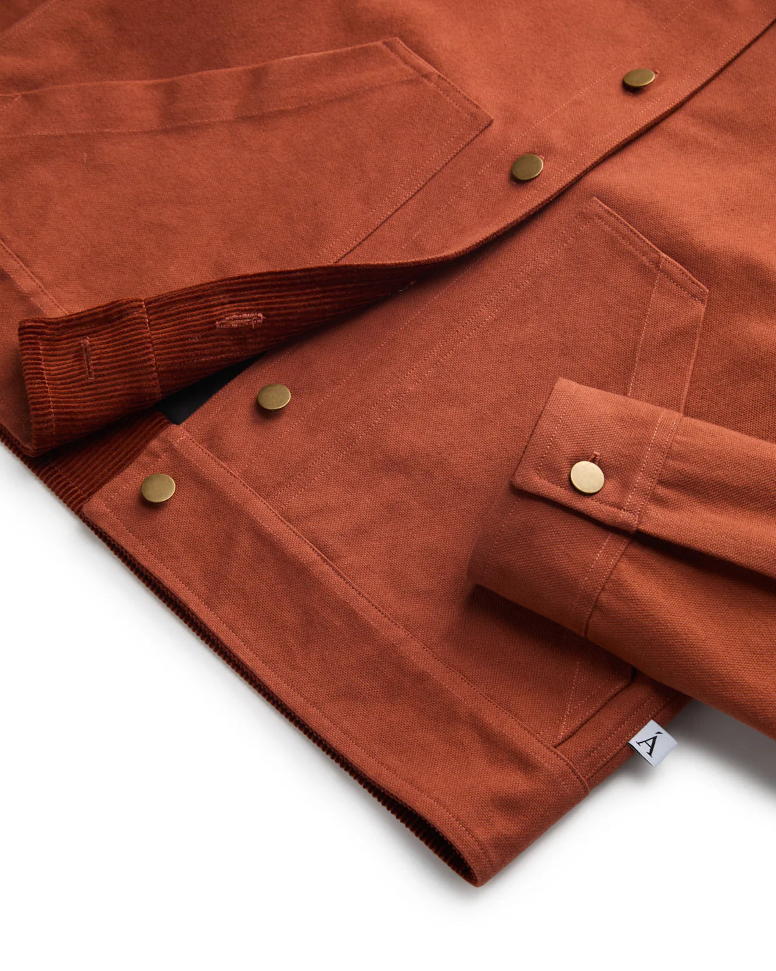 CLOSE UP FLAT LAY SHOT OF ONE CUFF, BRASS BUTTONS, AND HEMLINE DETAILS OF RED-ORANGE BARN COAT