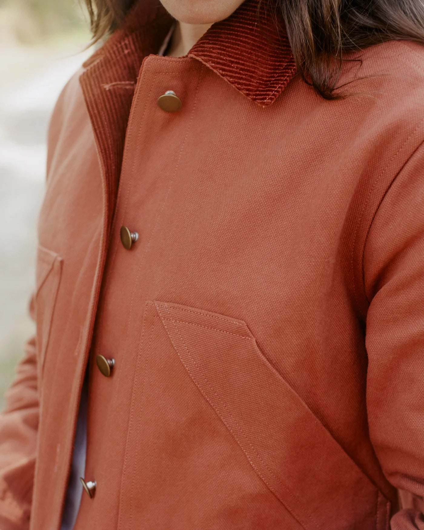 CLOSE UP MODEL SHOT OF RED-ORANGE BARN COAT - COLLAR, BUTTON, AND FRONT POCKET DETAILS