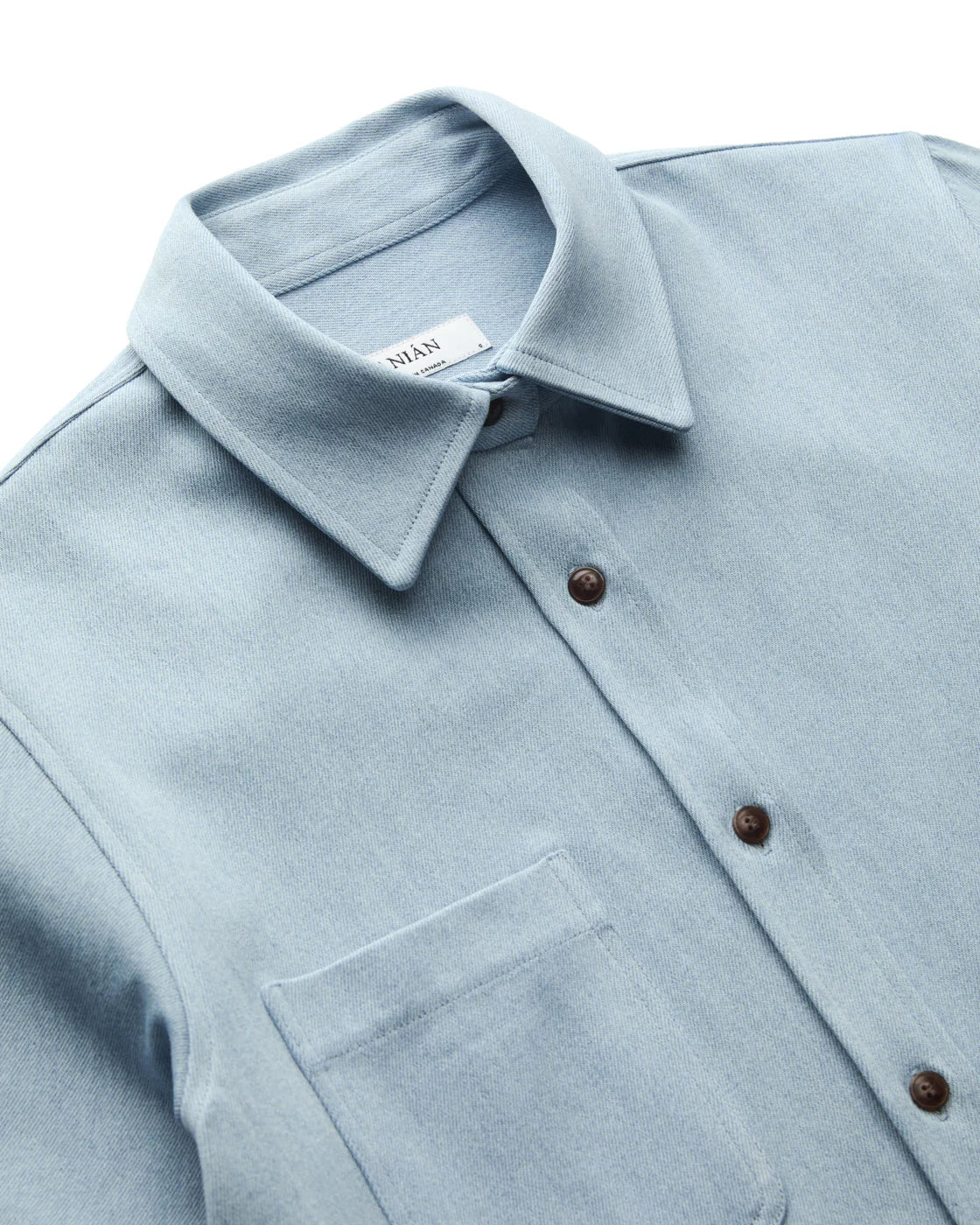 LIGHT BLUE DENIM SHIRT FLAY LAY CLOSEUP OF COLLAR AND BUTTONS AGAINST WHITE BACKGROUND