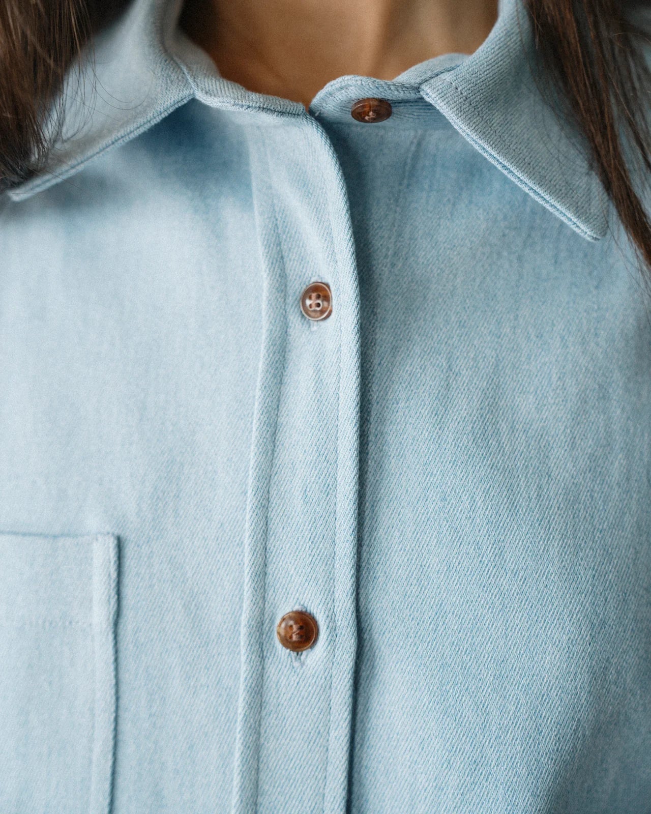 CLOSE UP COLLAR SHOT OF FEMALE MODEL WEARING LIGHT BLUE DENIM SHIRT