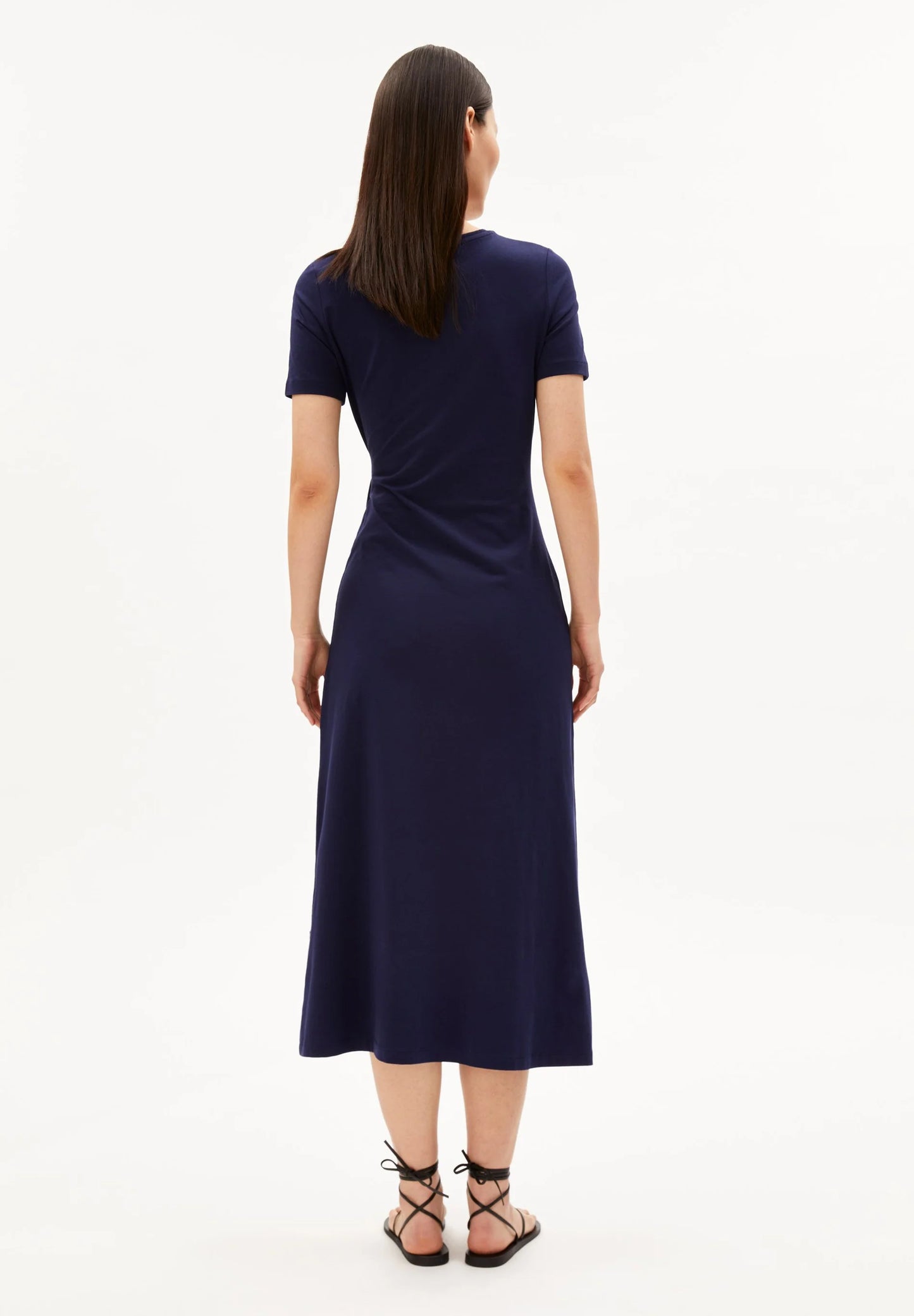 BACKSIDE OF NAVY SHEATH WRAP DRESS ON MODEL WITH BLACK HAIR AND FLAT SANDALS AGAINST WHITE BACKGROUND