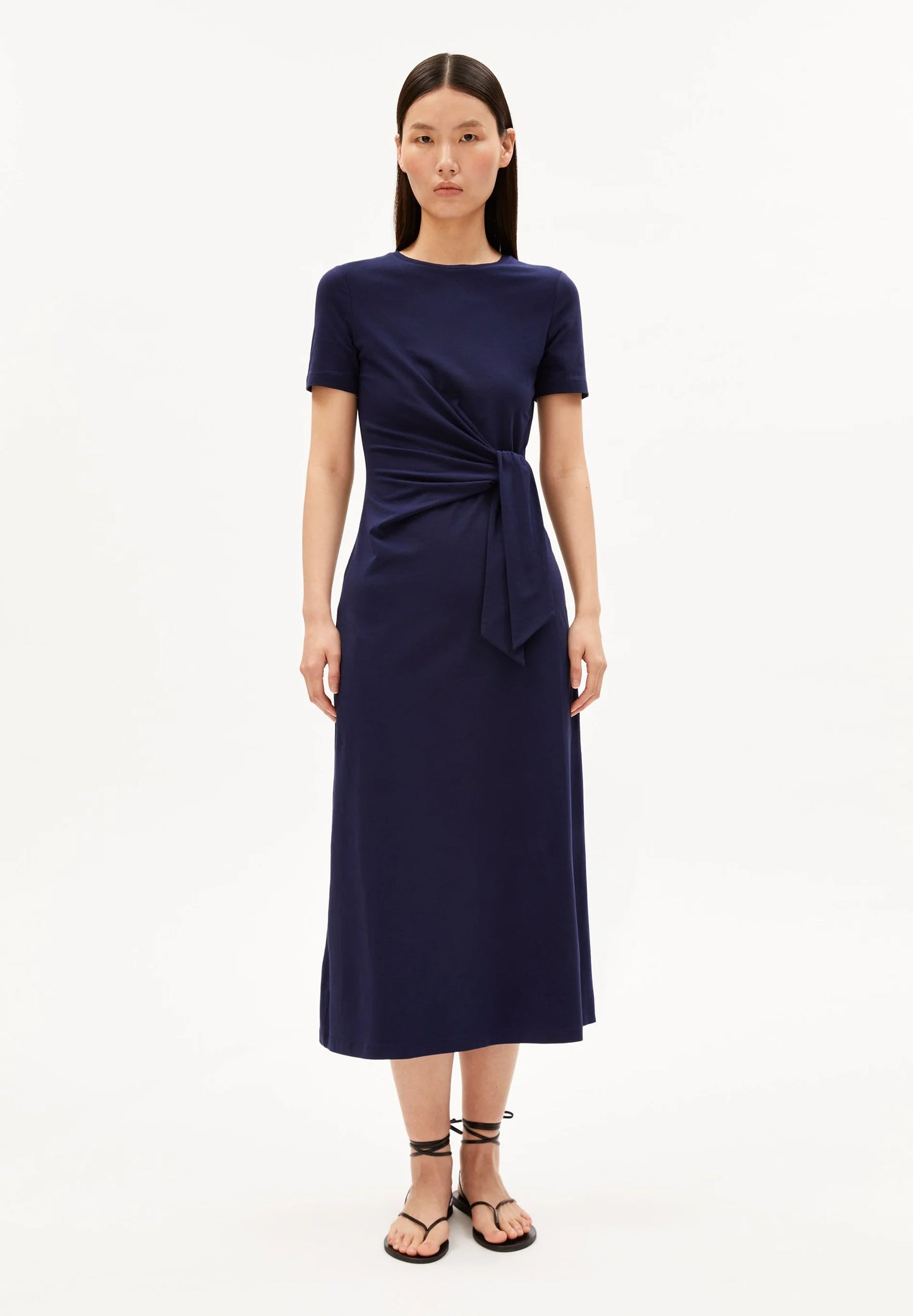 NAVY SHEATH WRAP DRESS ON MODEL WITH BLACK HAIR AND FLAT SANDALS AGAINST WHITE BACKGROUND