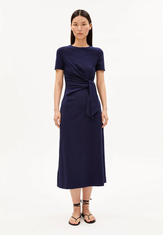 NAVY SHEATH WRAP DRESS ON MODEL WITH BLACK HAIR AND FLAT SANDALS AGAINST WHITE BACKGROUND