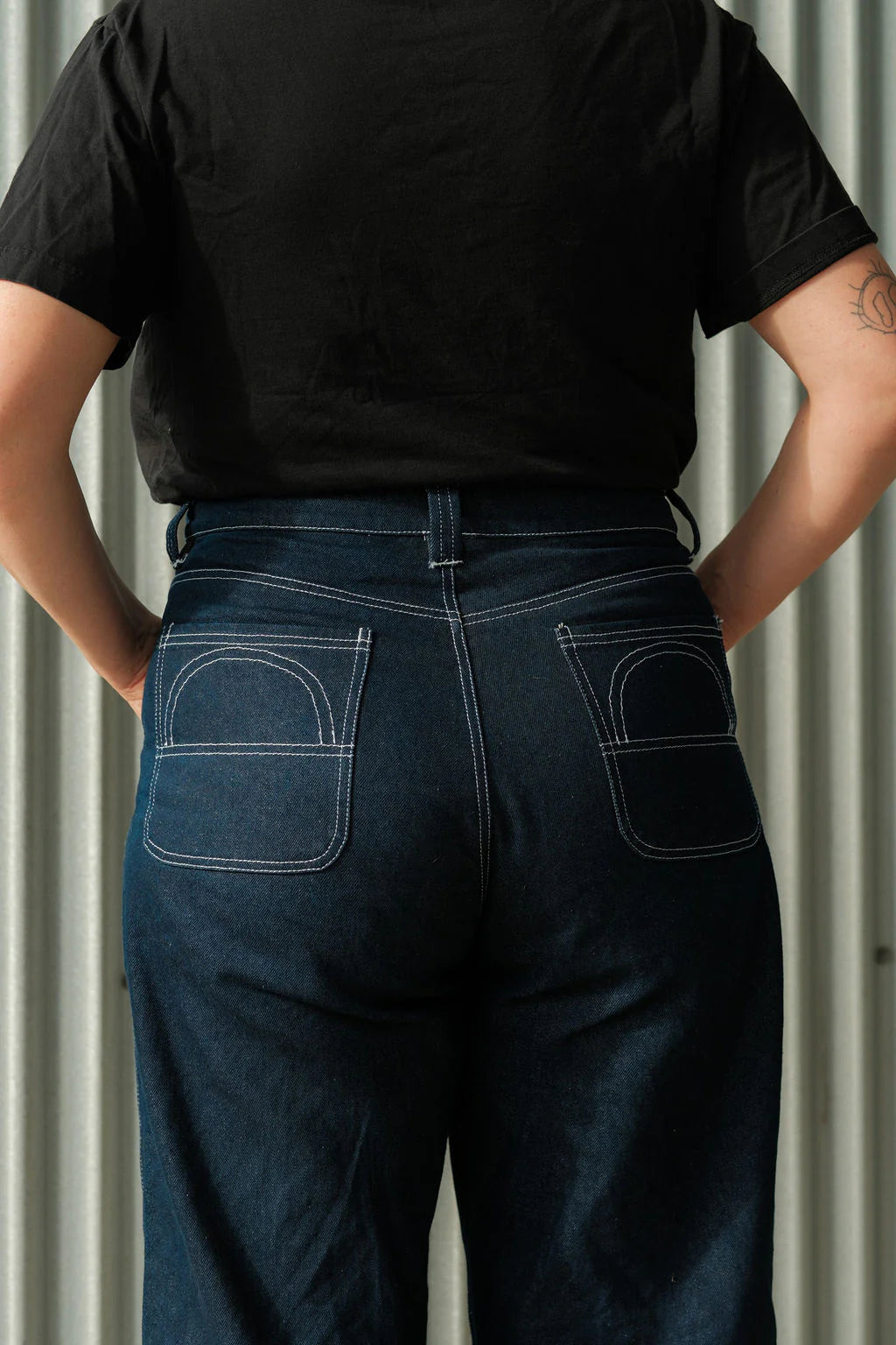 Person wearing a black t-shirt and dark blue jeans against a neutral background