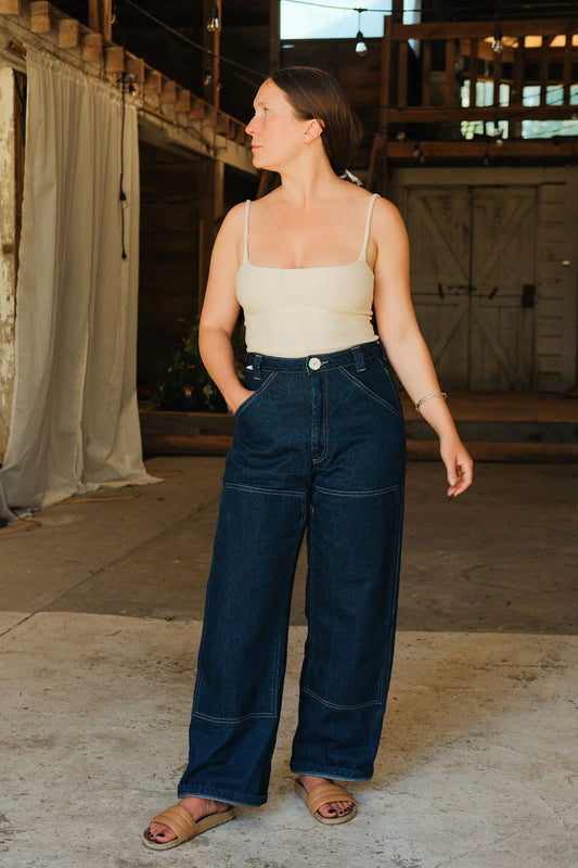 Woman wearing a beige tank top and blue jeans in an indoor setting