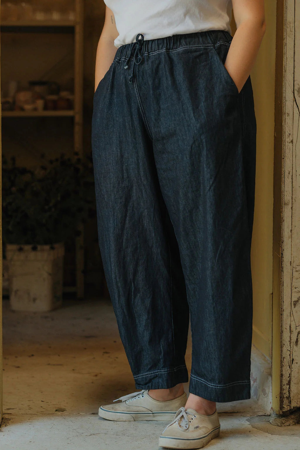 Person wearing dark blue pants and white sneakers in a rustic indoor setting