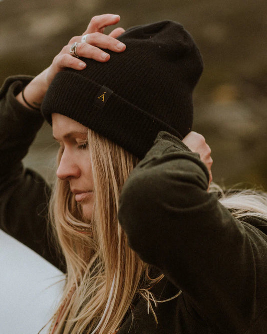 Anian black knit cuff wool oque on woman adjusting hat outdoors with long blonde hair and small gold logo in Kelowna