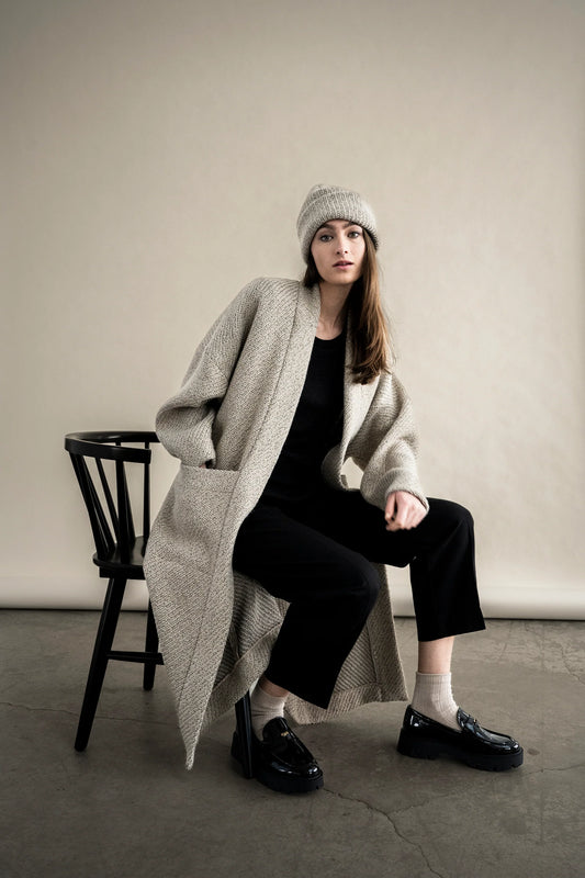 BodyBag by Jude long textured beige cardigan with pockets worn over black outfit and beanie while seated in Kelowna