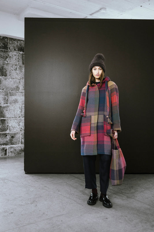 Model wearing a colorful plaid coat holding a matching tote bag in a modern indoor setting in Kelowna