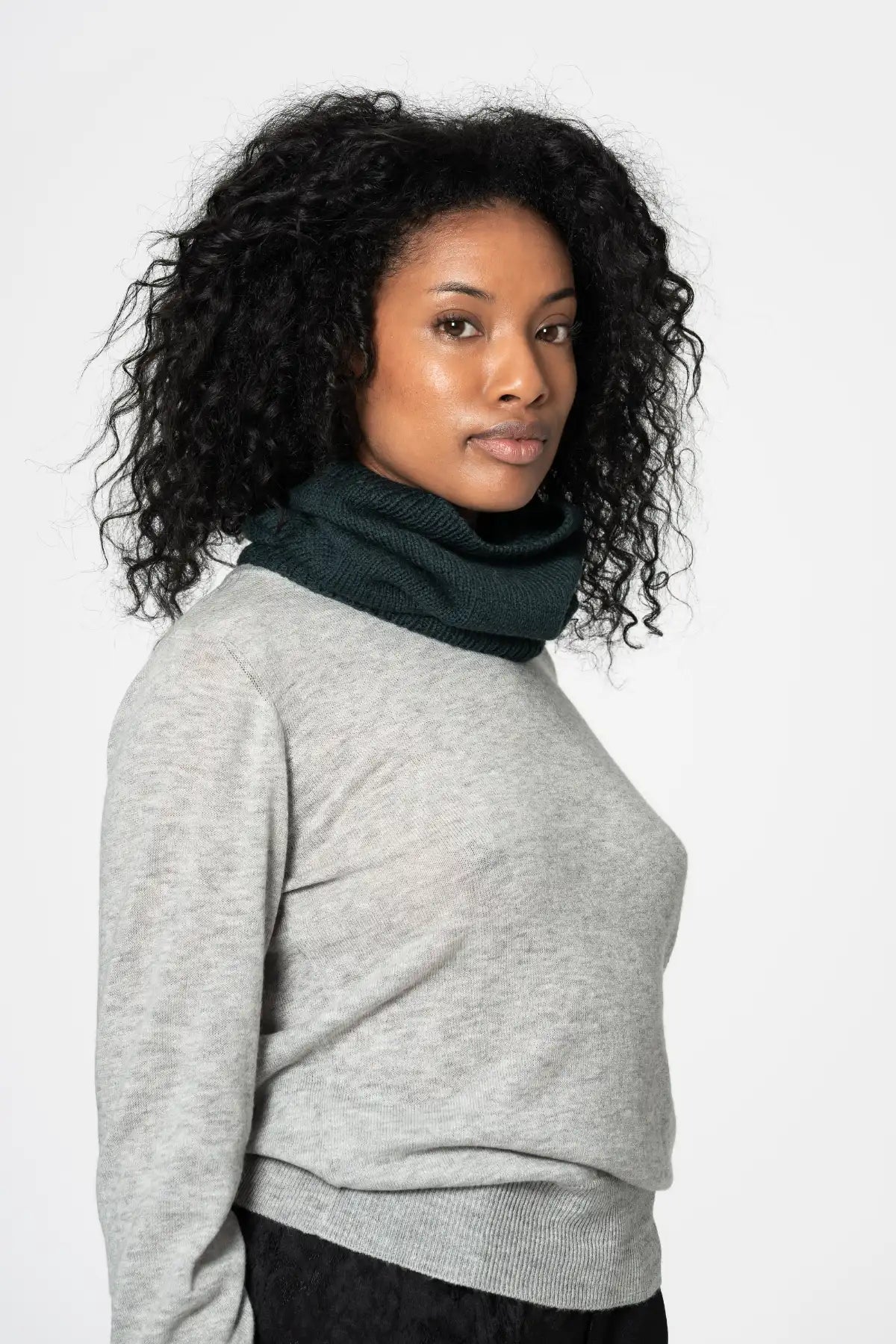 Dinadi neckwarmer in dark green merino wool worn stylishly by a woman with curly hair in Kelowna
