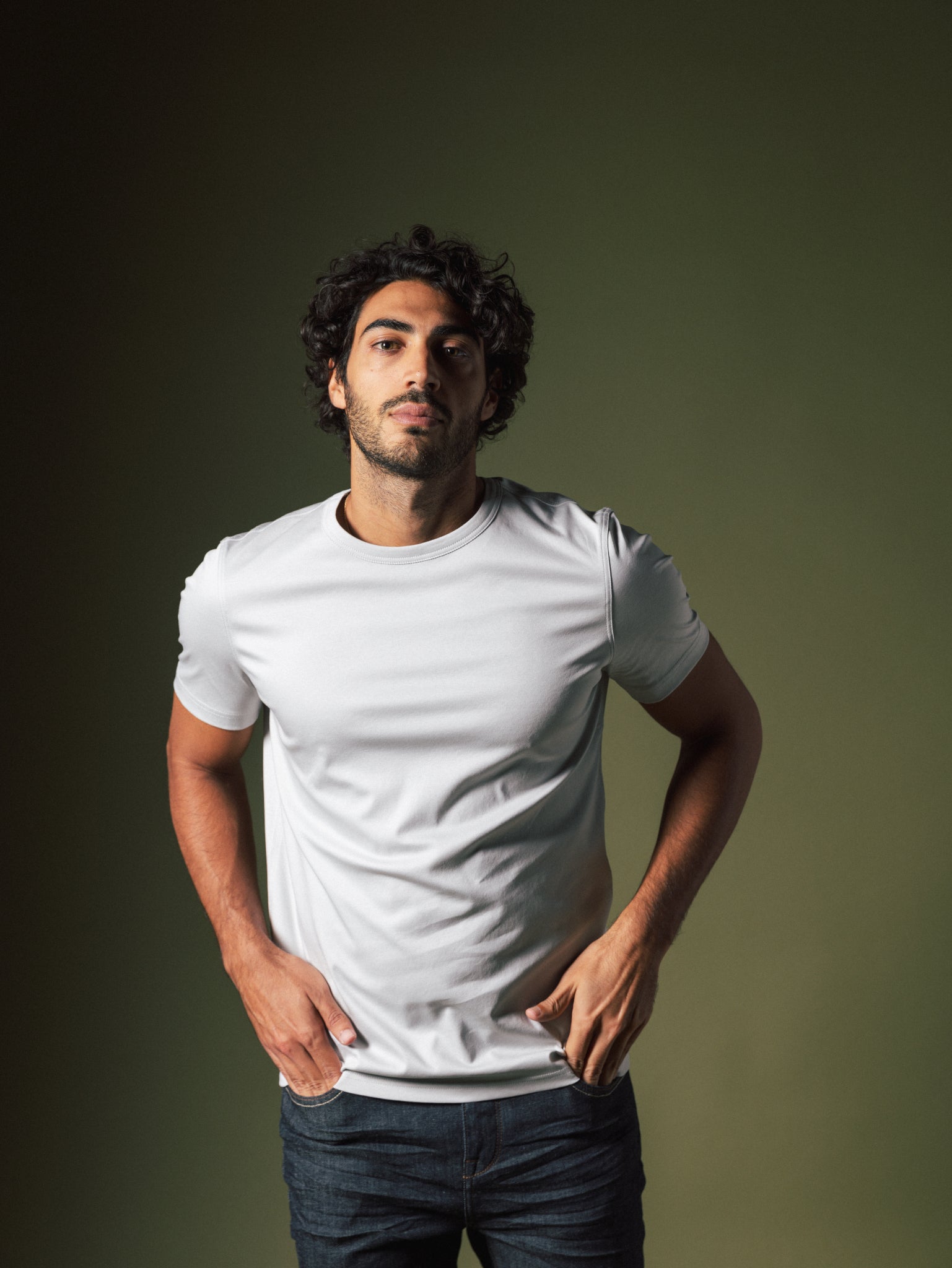 Male model wearing Mos Mosh Gallery organic gray t-shirt with dark jeans on green studio backdrop in Kelowna