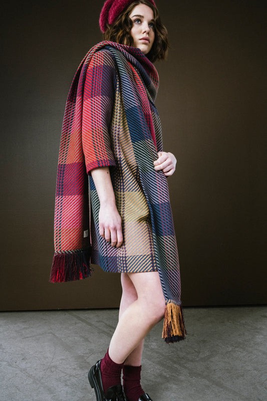 Model wearing a colorful plaid scarf with fringe edges, styled with a coordinating beret and chic outfit